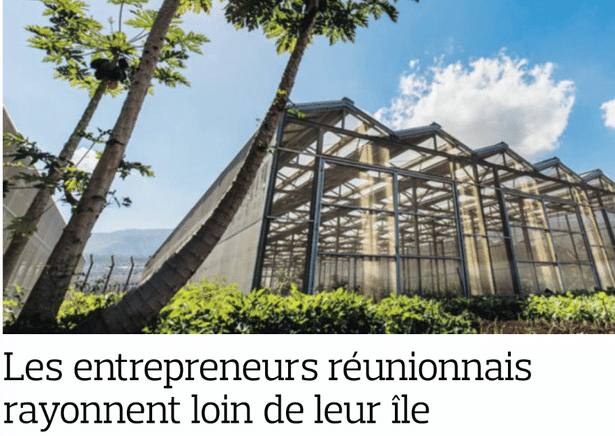 Serre moderne entourée de végétation sous un ciel bleu.