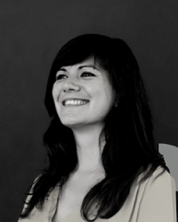 Femme souriante en noir et blanc sur fond sombre.