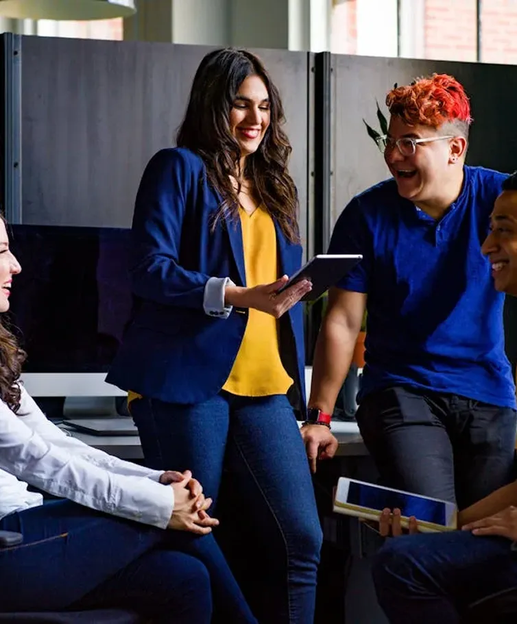 Quatre personnes discutent joyeusement autour d'une tablette dans un bureau.