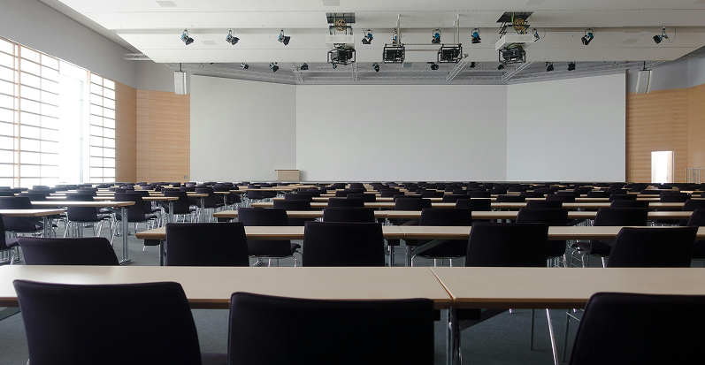 Salle de conf&eacute;rence vide avec rang&eacute;es de tables et chaises.