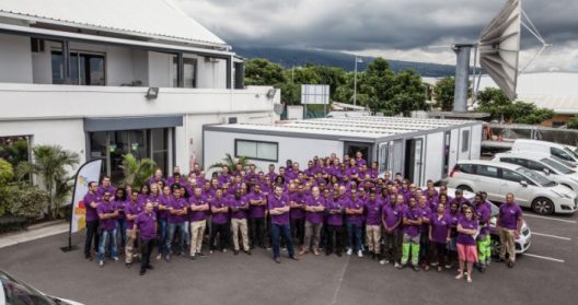 Groupe de personnes en chemises violettes posant devant un bâtiment.