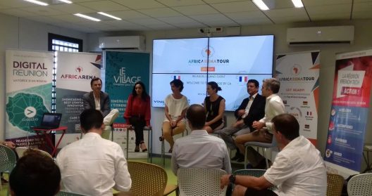 Des personnes discutent lors d'un événement AfricArena avec des affiches en arrière-plan.