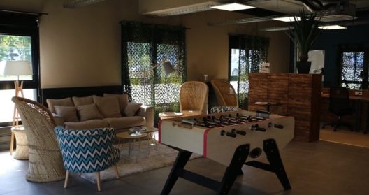 Salle de détente avec canapé, fauteuils en rotin et baby-foot.