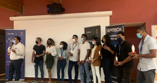 Groupe de personnes masquées tenant des trophées, debout devant des bannières d'événement.