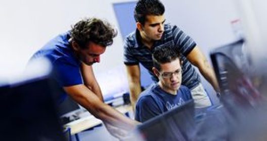 Trois hommes travaillant ensemble sur un ordinateur dans un bureau.
