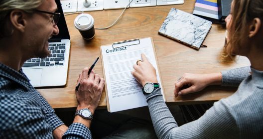 Deux personnes discutant d'un contrat à une table avec un ordinateur portable.